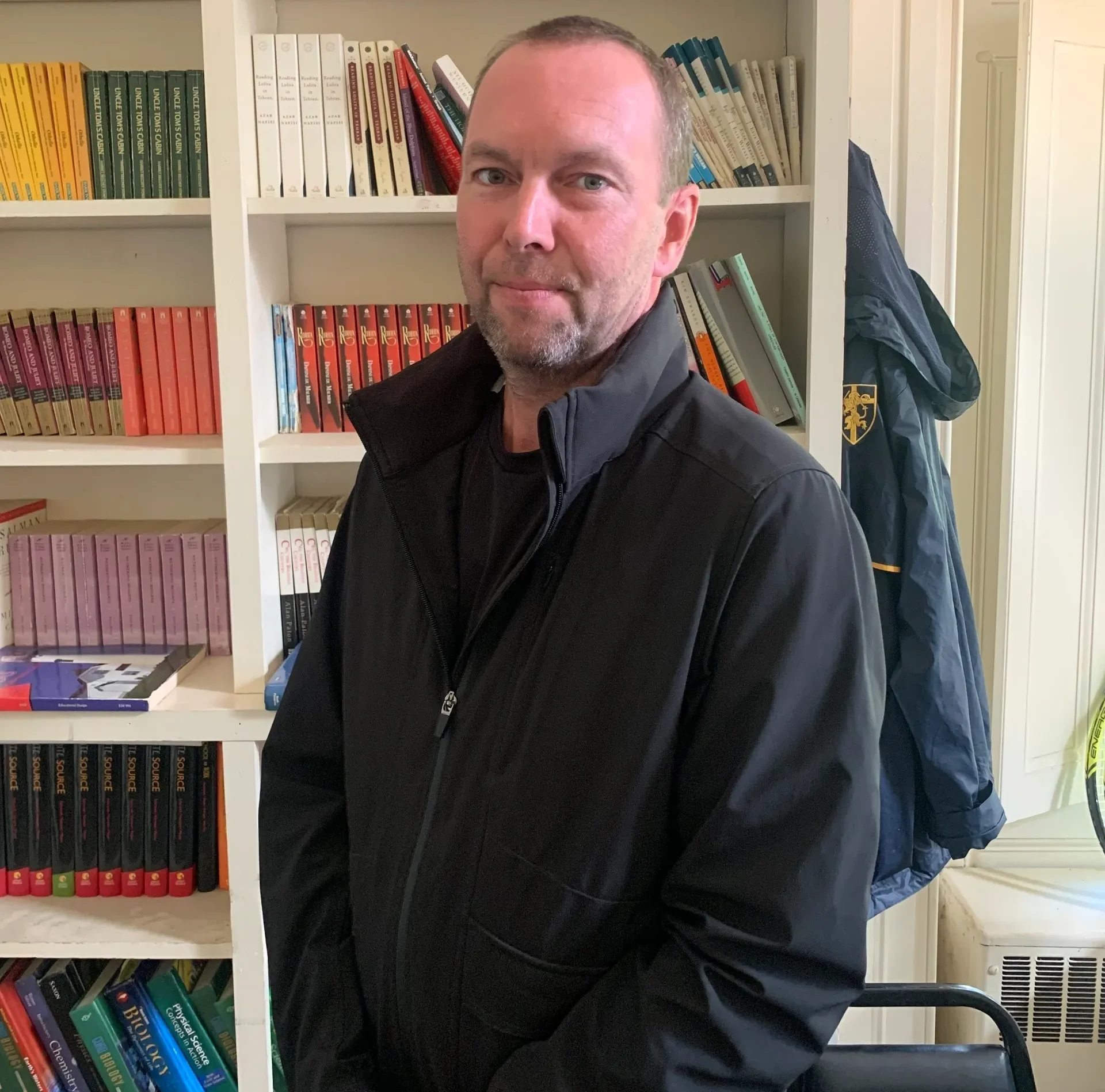 Man in black jacket near bookshelves.