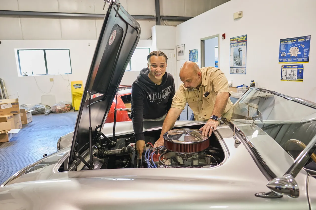 Mechanic and student working on car engine.