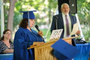 A woman in blue cap and gown speaking at a podium.