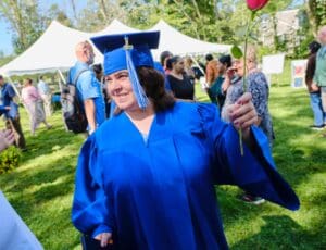 A woman in blue cap and gown holding her hand up.