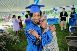 A man and woman in graduation attire hugging.