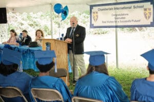 A man in blue cap and gown giving a speech.