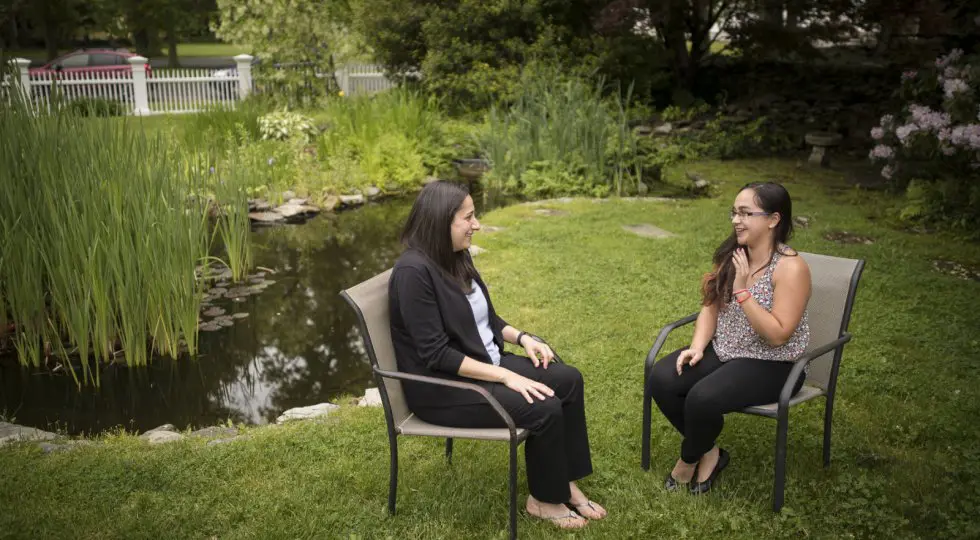 Two women sitting on chairs in a field.