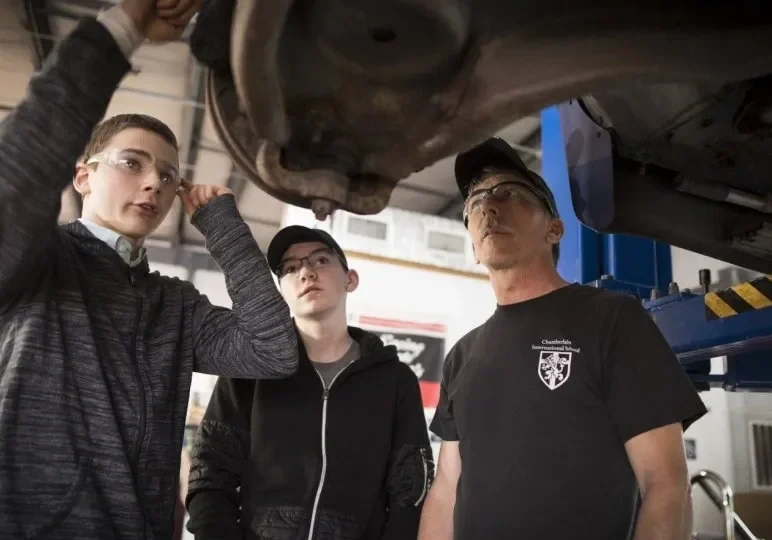 Mechanic instructing students on car repair.