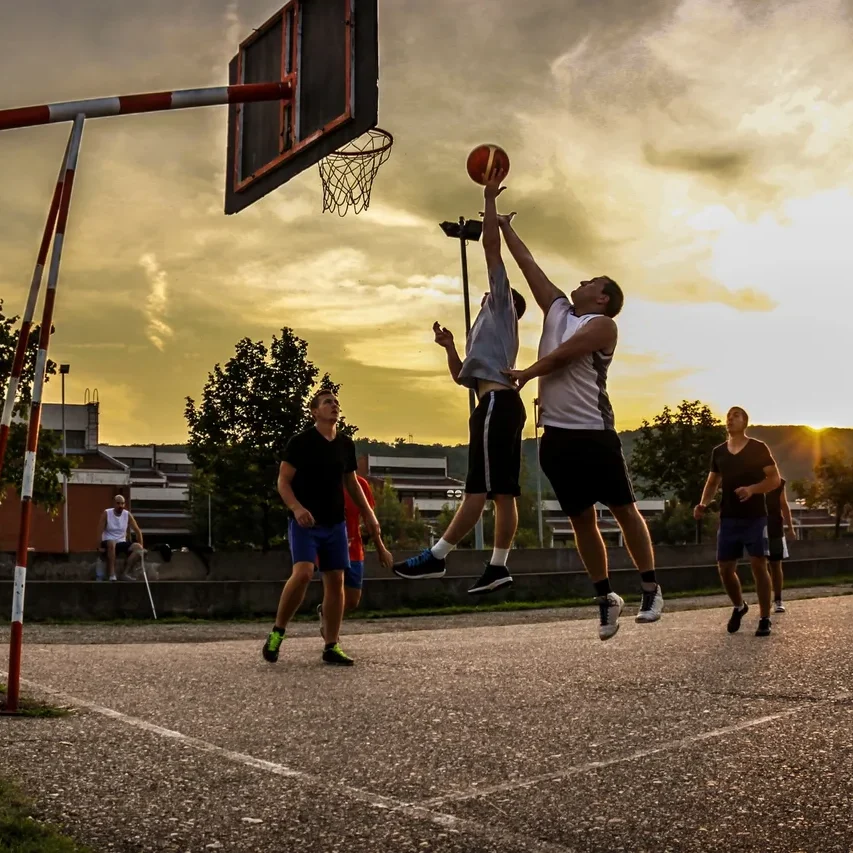 Men playing basketball at sunset.